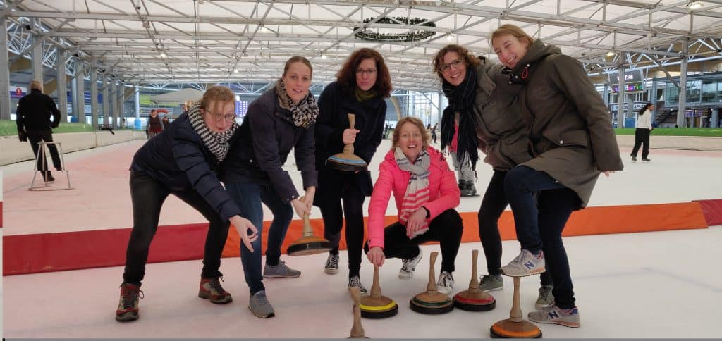 Leden van een bedrijfsteam spelen met elkaar Bavarian curling op de ijsbaan